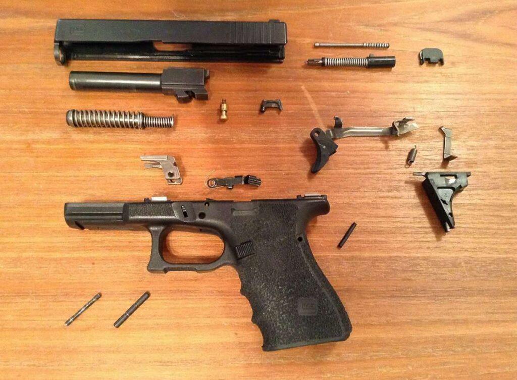 Disassembled pistol laid out on a wooden table: slide, barrel, springs, frame, and small parts visible. - Glock Maintenance Checklist: Cleaning, Lubrication & Inspection Tips , Mid State Firearms