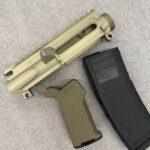 Tan AR-style rifle upper receiver with a Picatinny rail and a black magazine nearby on carpeted surface, shown in close-up. - Gold/Tan Forged Slick Side AR-15 Stripped Upper Receiver , Mid State Firearms
