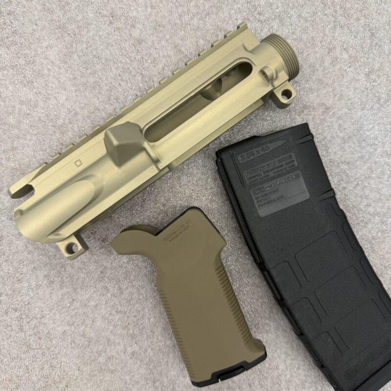 Tan AR-style rifle upper receiver with a Picatinny rail and a black magazine nearby on carpeted surface, shown in close-up. - Gold/Tan Forged Slick Side AR-15 Stripped Upper Receiver , Mid State Firearms